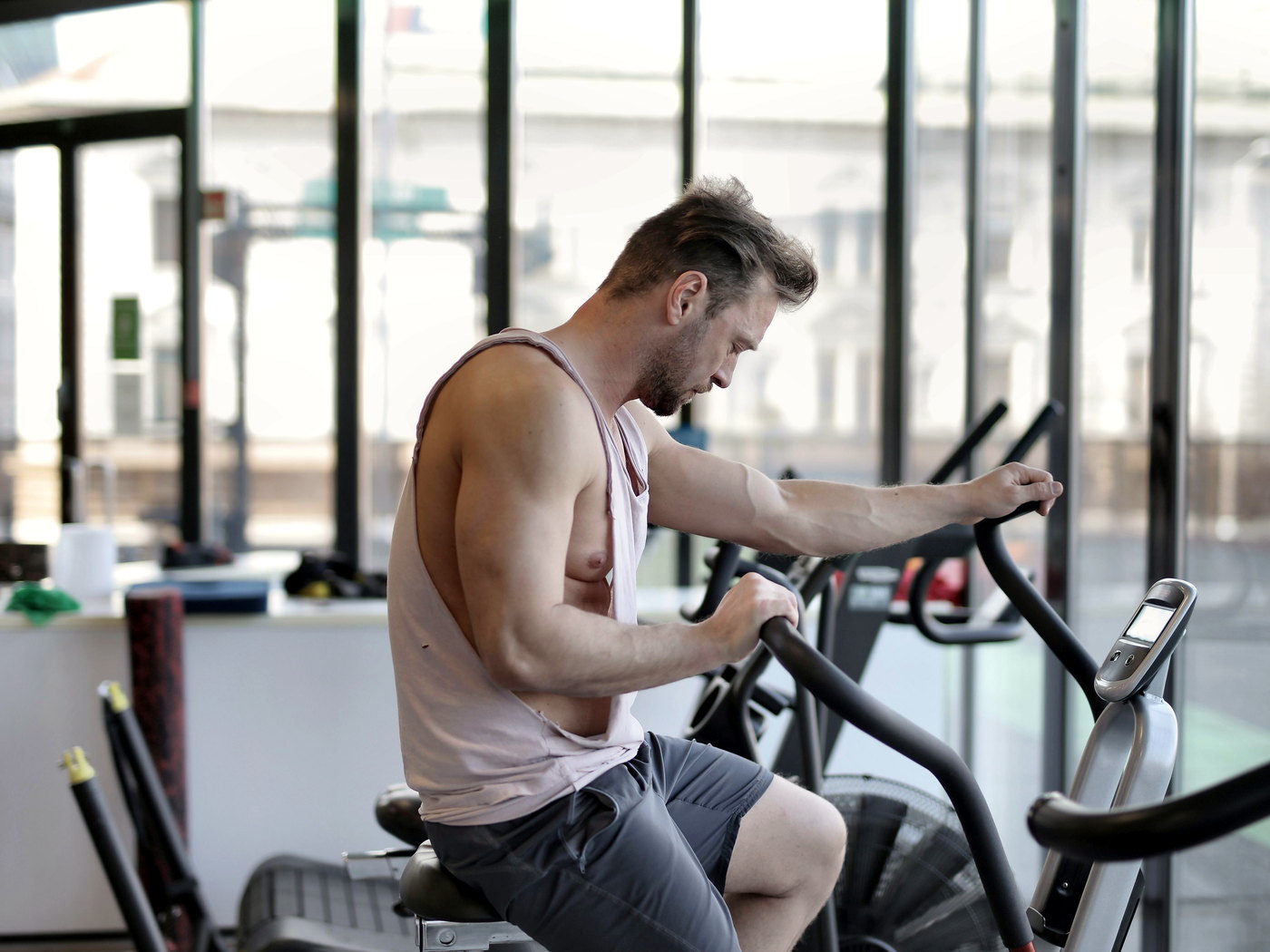 Man training on a cardio machine in a gym beside a window, with other gym equipment nearby.